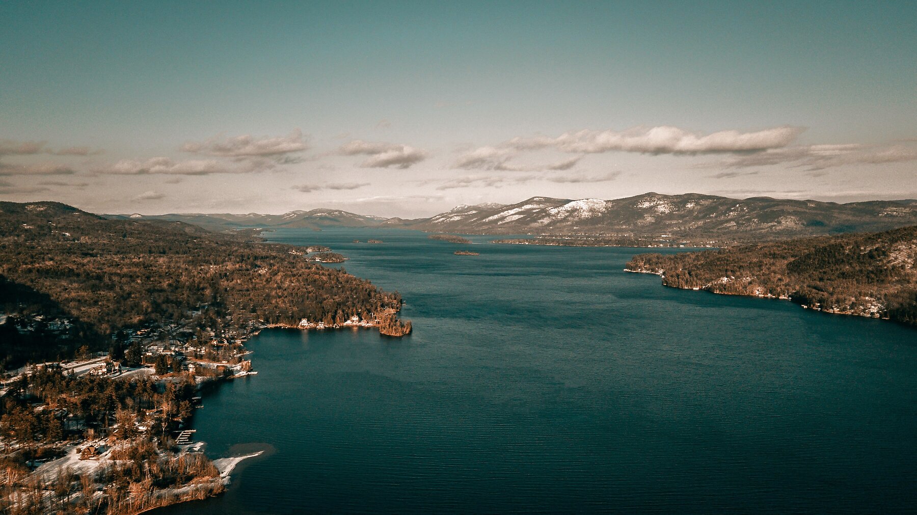 An aerial view of Lake George stretching between forested summer shorelines in the Adirondacks.