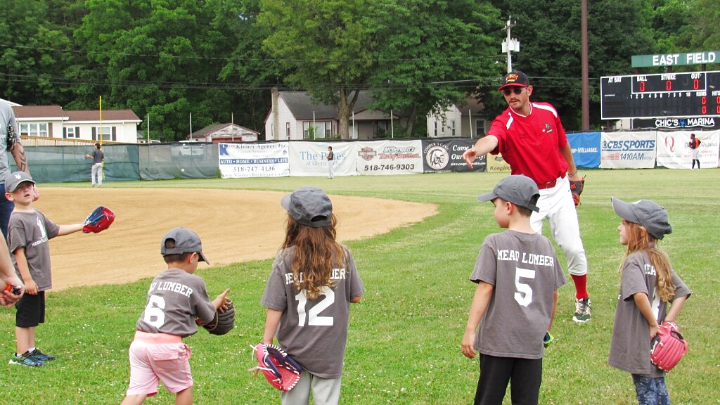 A Glens Falls Dragons player playing catch with a youth team on the field at East Field